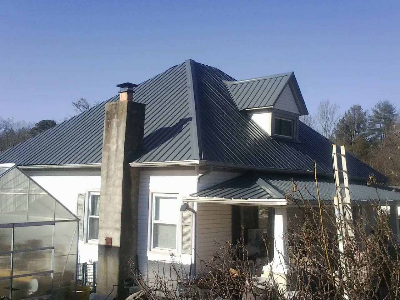 Dark blue standing seam metal roof on a white farmhouse with dormer — Slate & Tile Roof Repair by Roofing Brothers in Lytle Creek