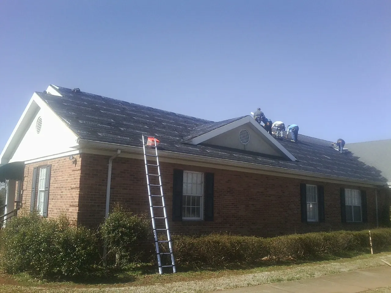 Crew tearing shingles off a brick ranch roof with a ladder set — Emergency Roof Repair work by our crew in Lytle Creek