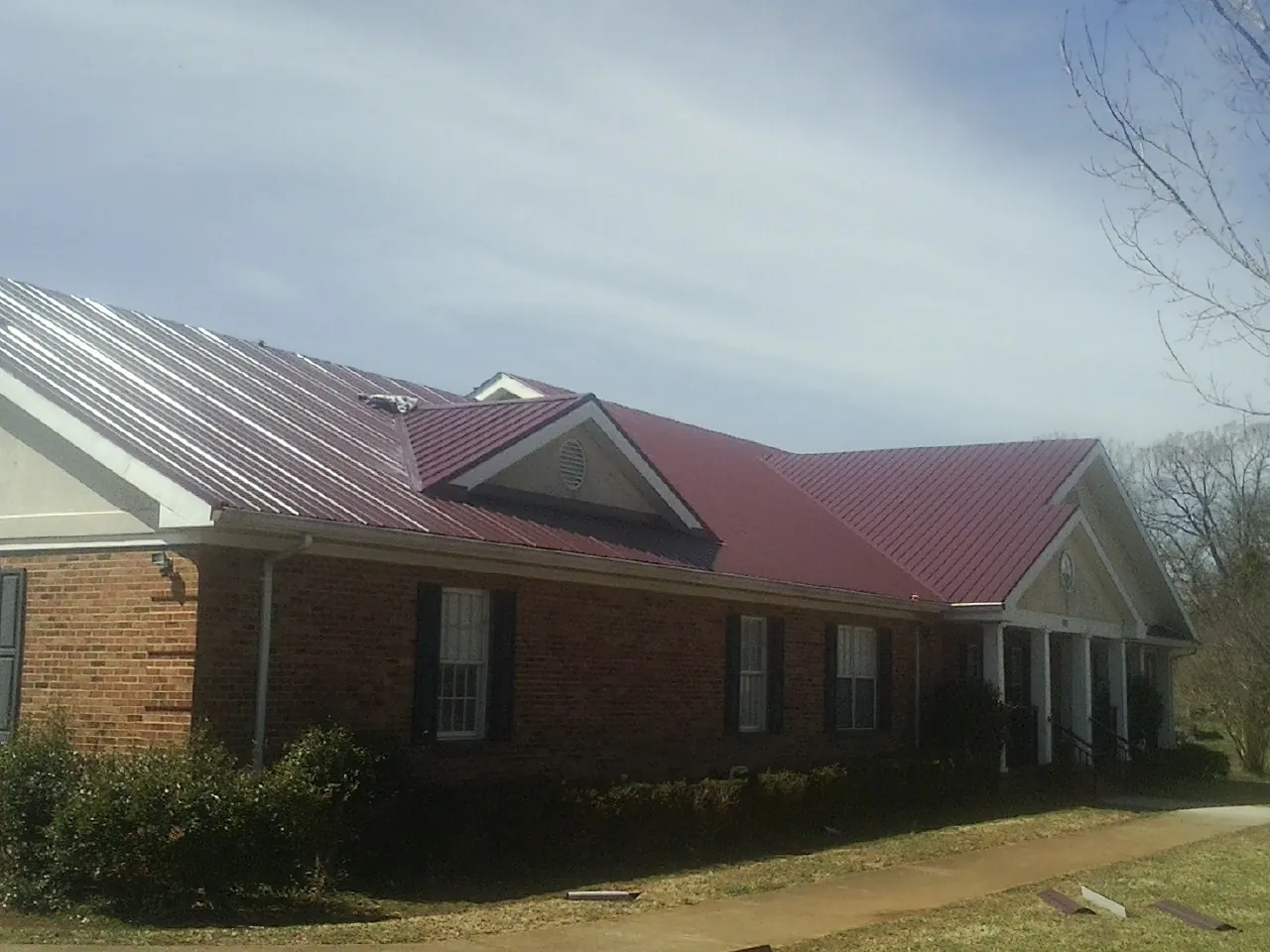 Red metal roof with gabled entries on a long brick building, from a Hail Damage Roof Repair job in Lytle Creek